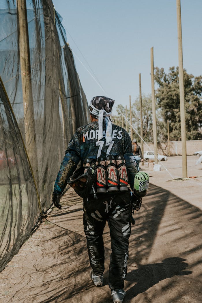 Paintball player in full gear walking on an outdoor field, equipped for a game.